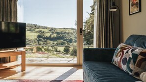 Ein Wohnzimmer mit Fernseher, einer Couch und Blick auf eine grüne Landschaft durch eine Glastür.