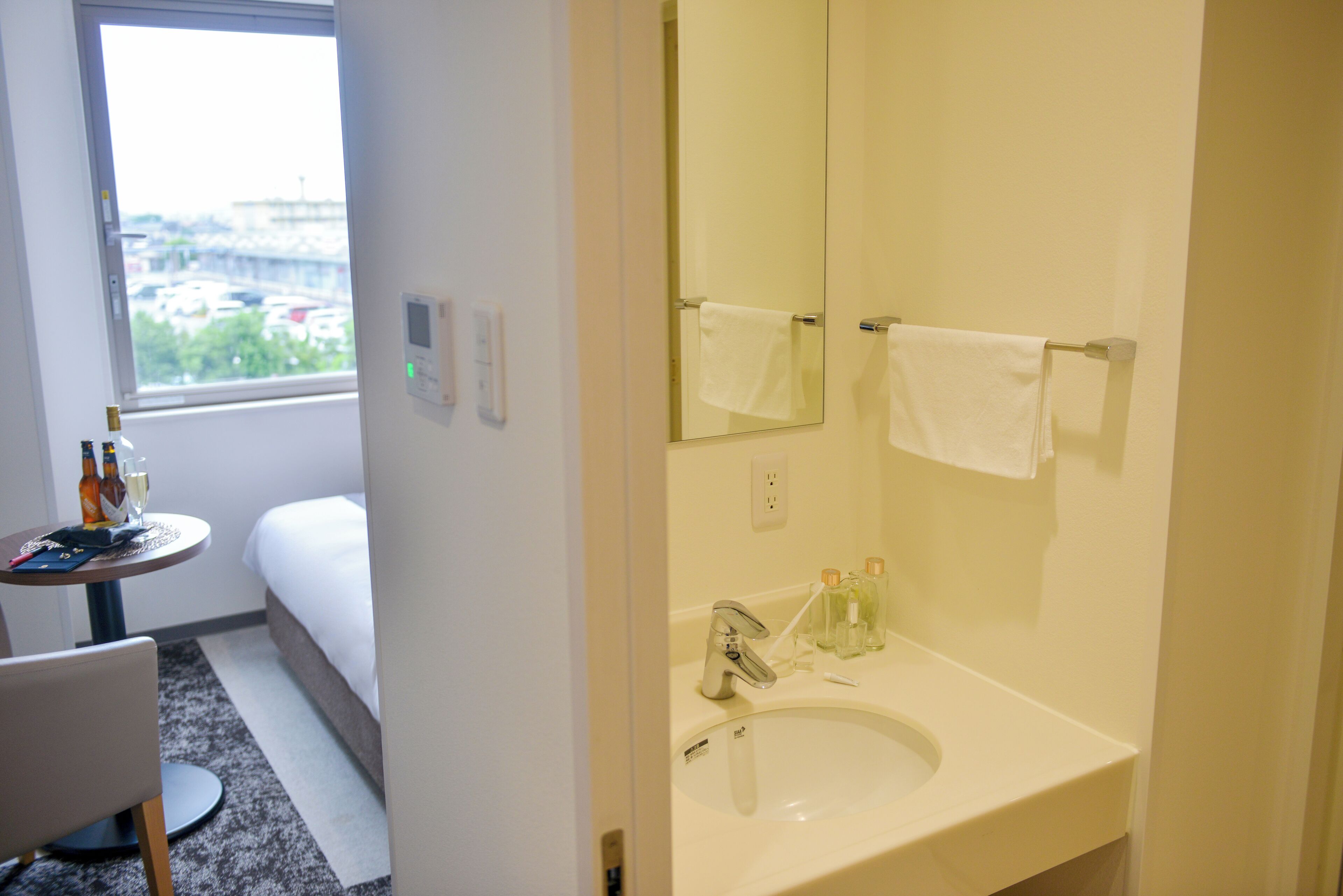 A hotel bathroom with a sink, mirror, towel rack, and a window with a view of buildings.