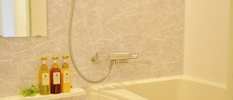 A bathroom with a bathtub, a shower head, and a shelf with toiletries.