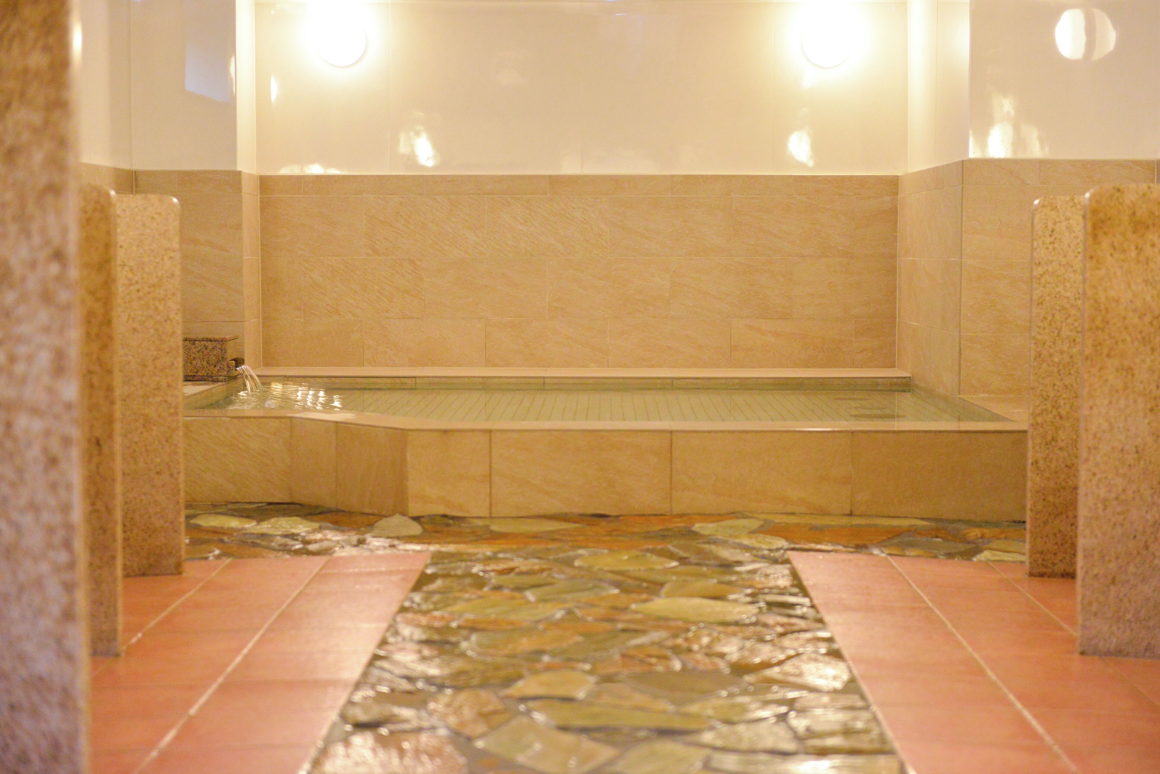 A bathroom with a stone mosaic floor, a bathtub, and a tiled wall.