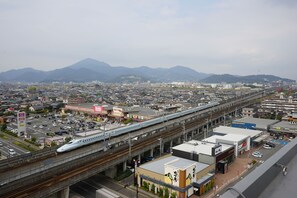 A high-speed train passing over an elevated highway with a cityscape and mountains in the background.