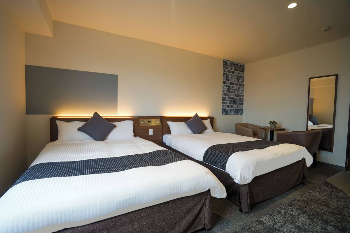 A hotel room with two beds, a desk, a chair, a small table, and a mirror.