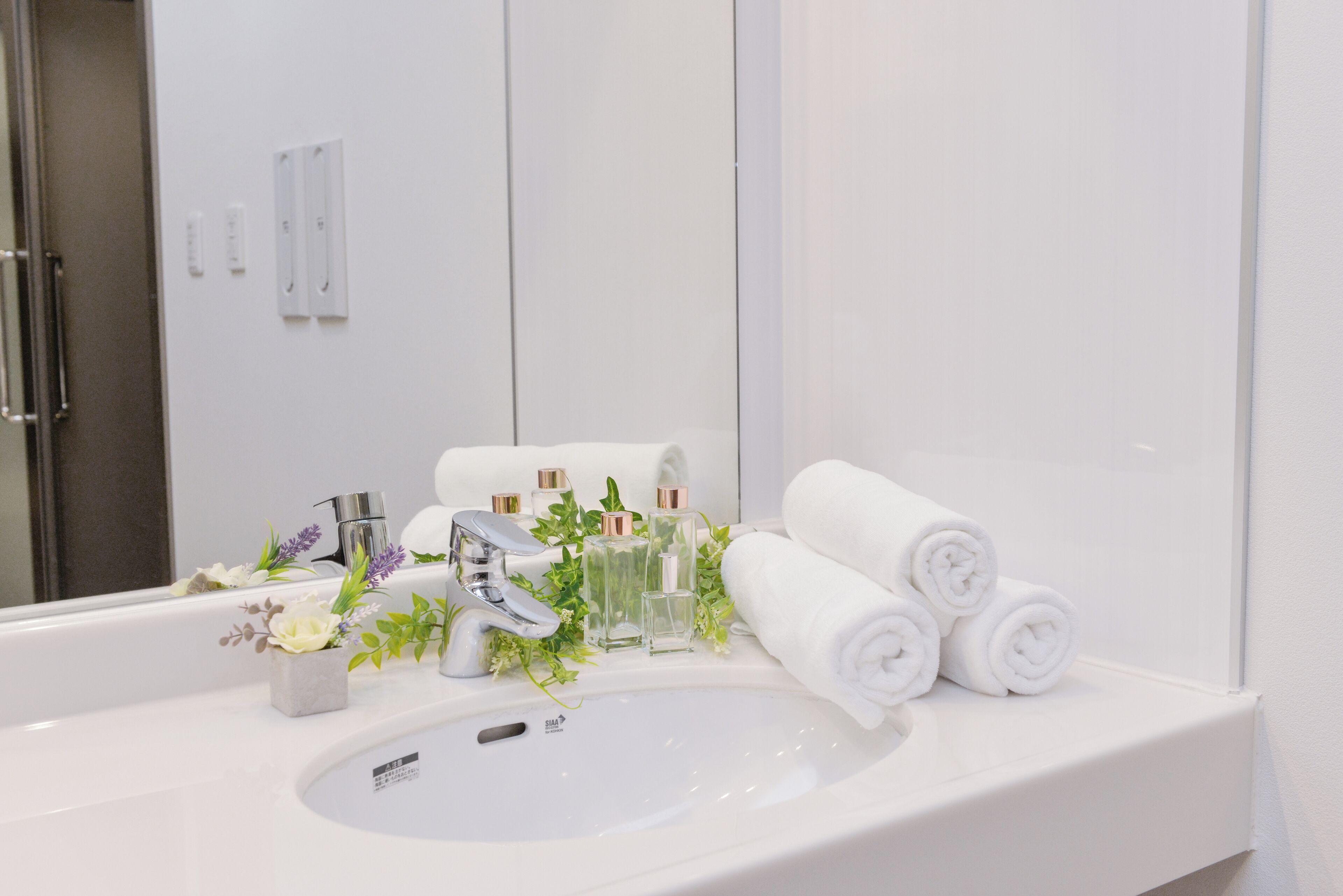 A bathroom with a white sink, two faucets, a mirror, and neatly rolled towels.