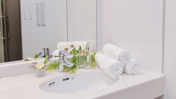 A bathroom with a white sink, two faucets, a mirror, and neatly rolled towels.