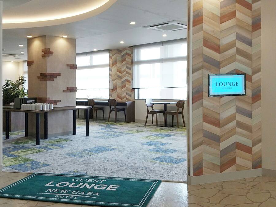 Um hall de hotel com parede em padrão losango, balcão de recepção e diversas áreas de estar.