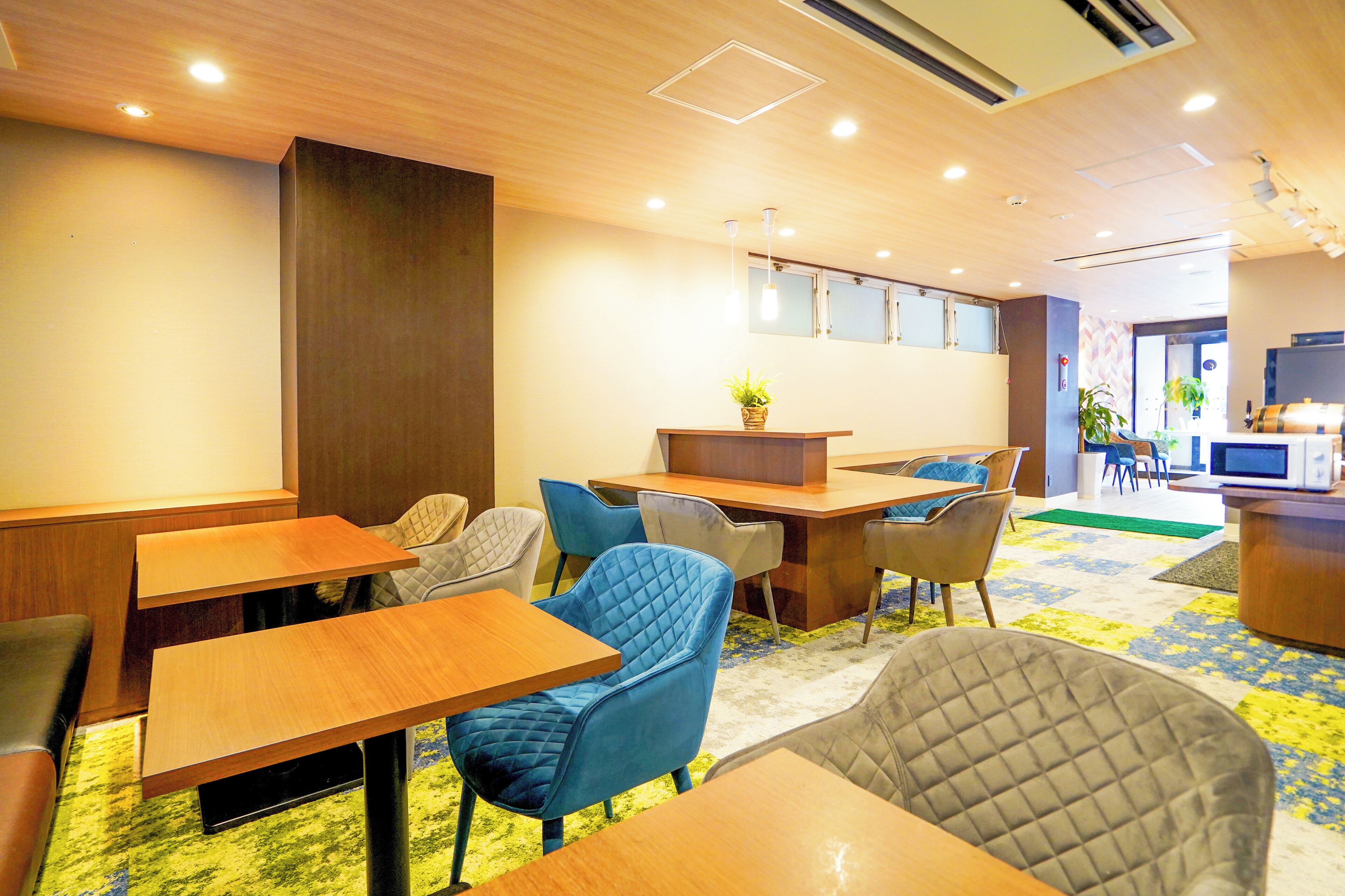A modern hotel lobby with wooden tables and chairs, a reception desk, and a television.
