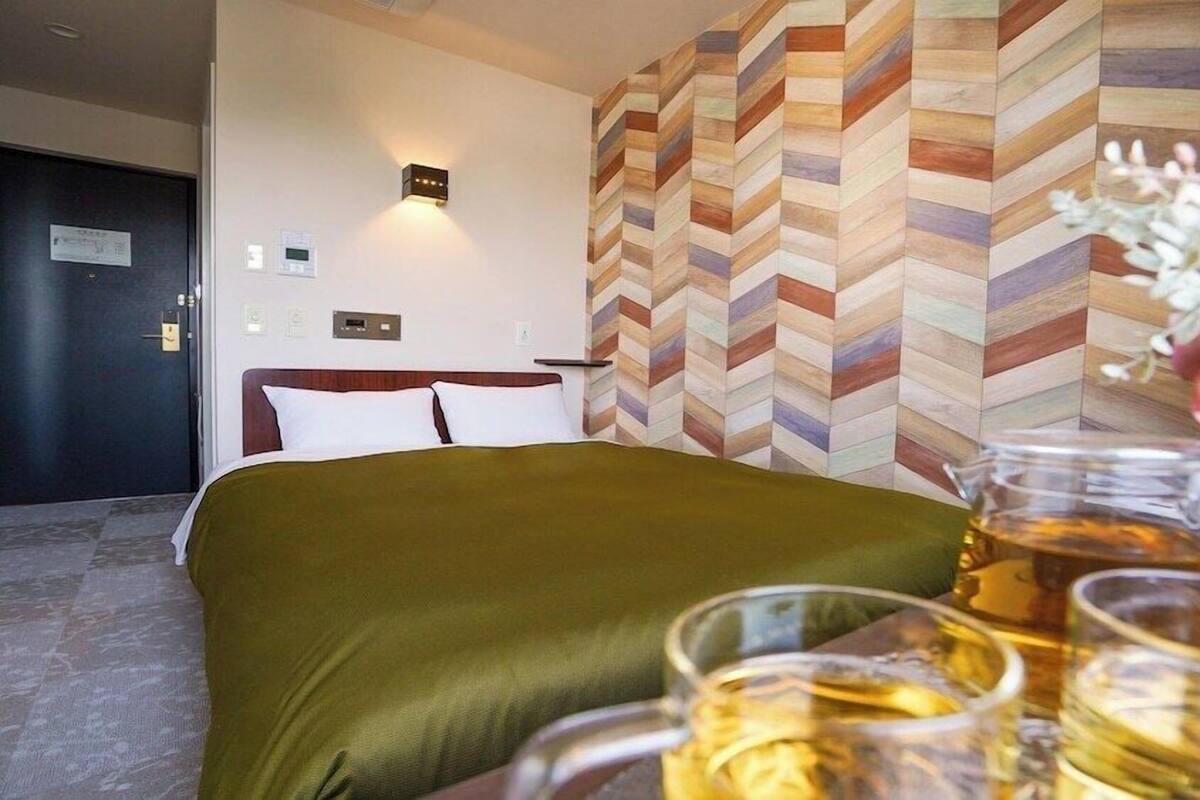 A hotel room with a bed, a wall with a chevron pattern, a bedside table with a vase of flowers, and a glass of beer.