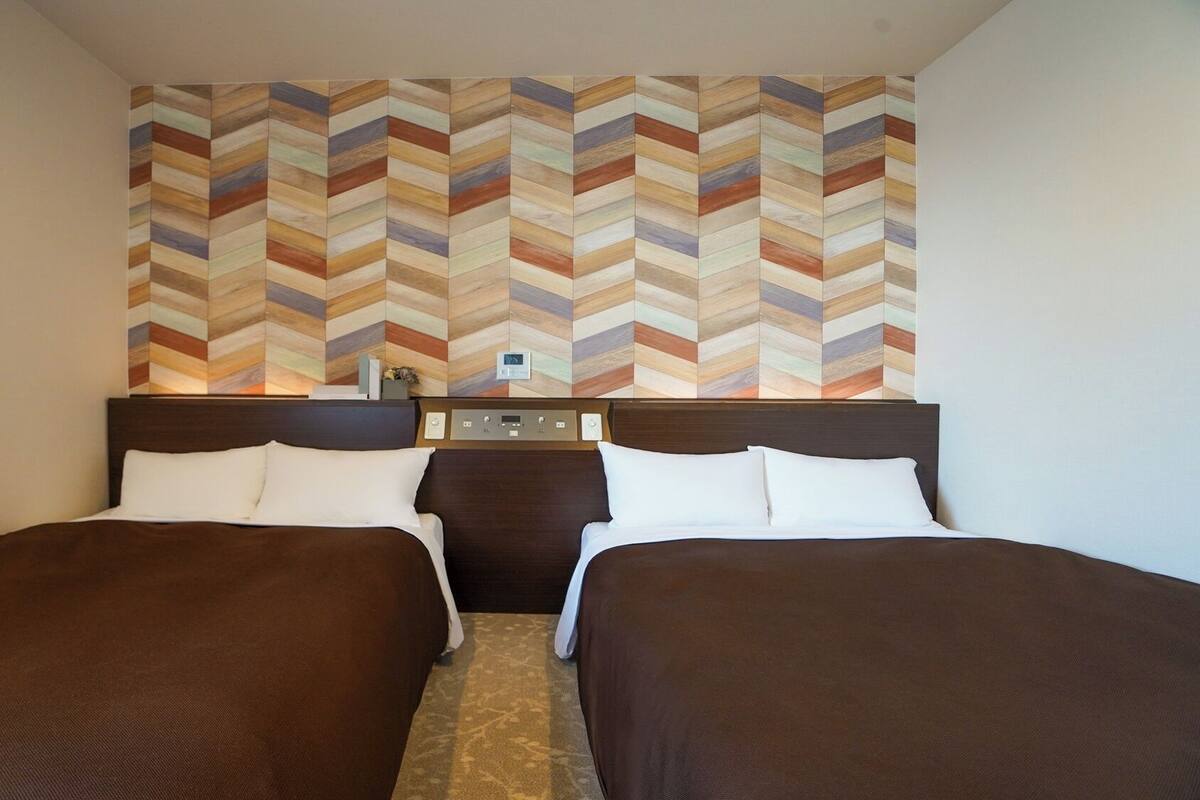 A hotel room with two beds, a control panel, and a chevron-patterned wall.