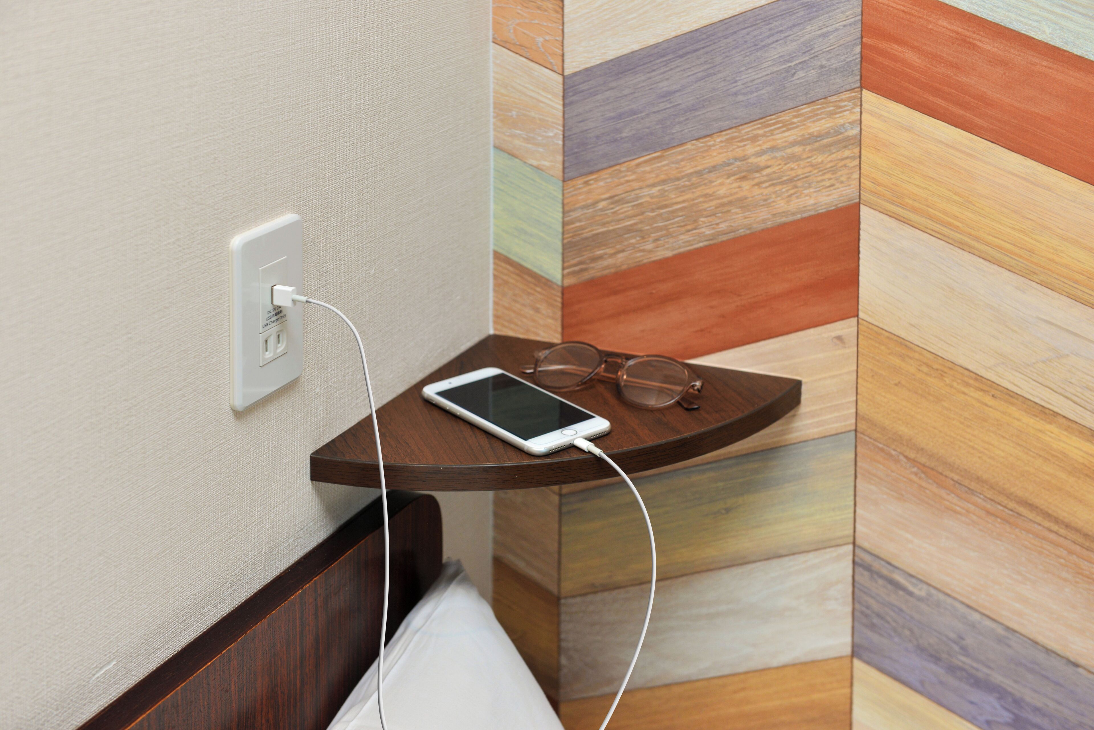 A smartphone charging on a wooden side table next to a wall socket.