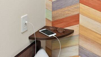 A smartphone charging on a wooden side table next to a wall socket.