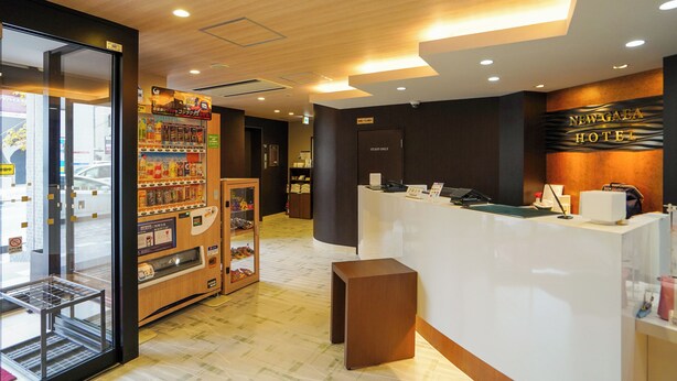 Zona de recepción de hotel con diseño moderno, que incluye un mostrador de recepción, máquinas expendedoras y una puerta con la indicación 