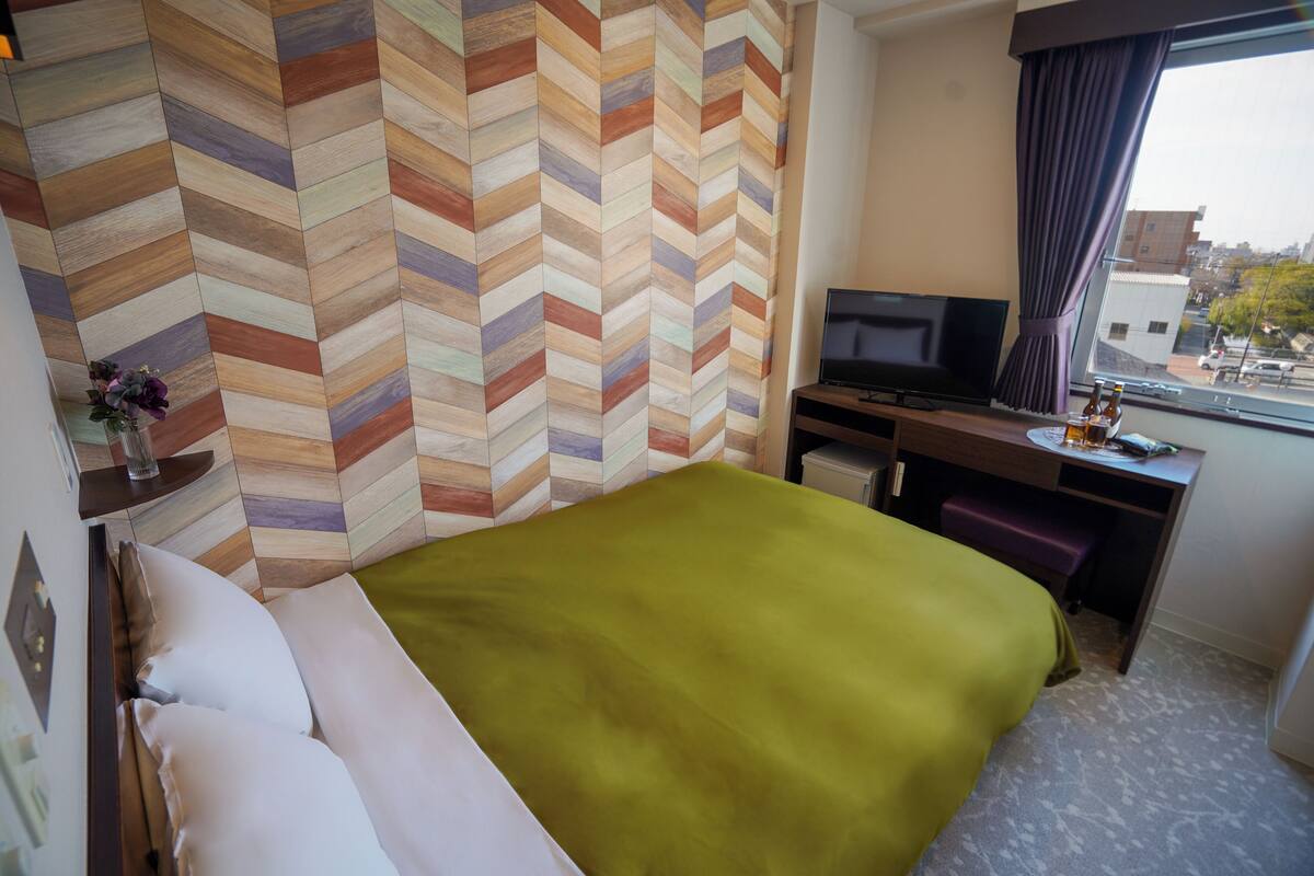A hotel room with a bed, a television, a desk, and a window with a view of the city.