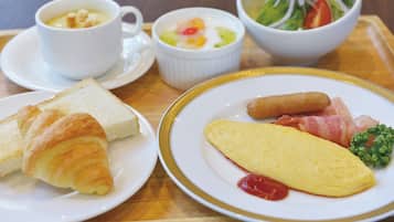 A tray with breakfast items including croissants, an omelette, sausages, and a bowl of salad.