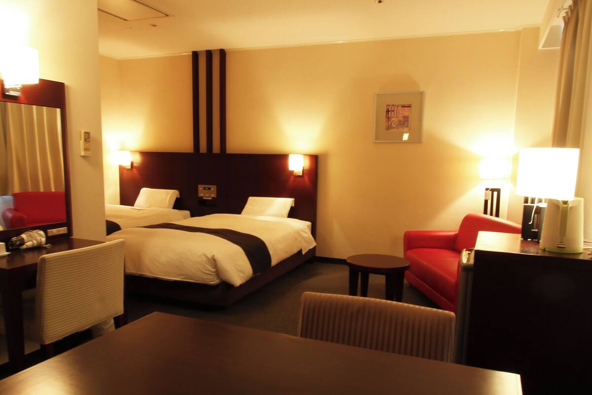 A hotel room with a large bed, a desk, a chair, a small table, and a red sofa.