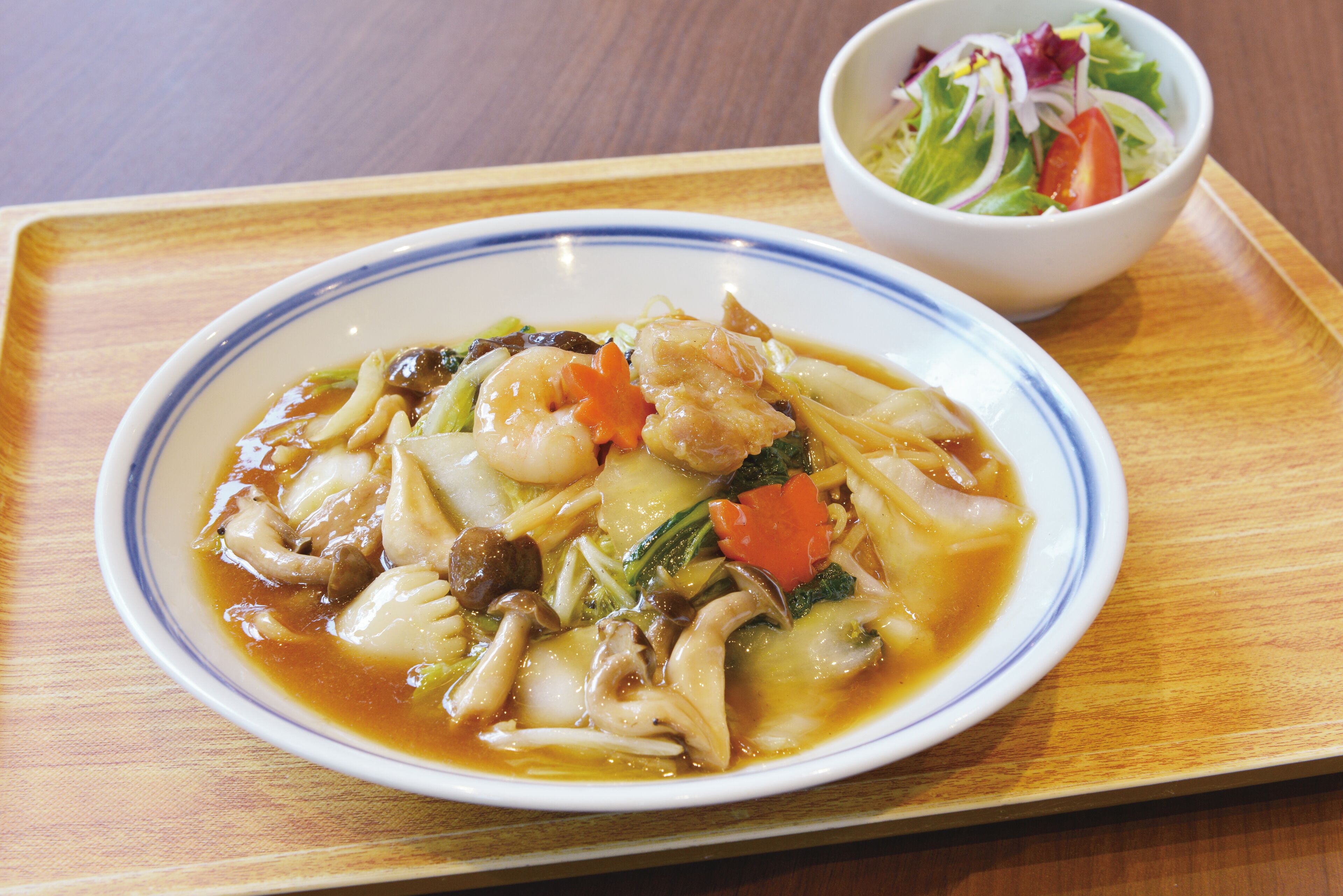 A plate of soup with vegetables and meat, and a side salad on a wooden tray.