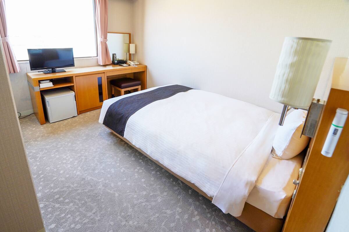 A hotel room with a bed, a desk with a computer, a telephone, and a small refrigerator.