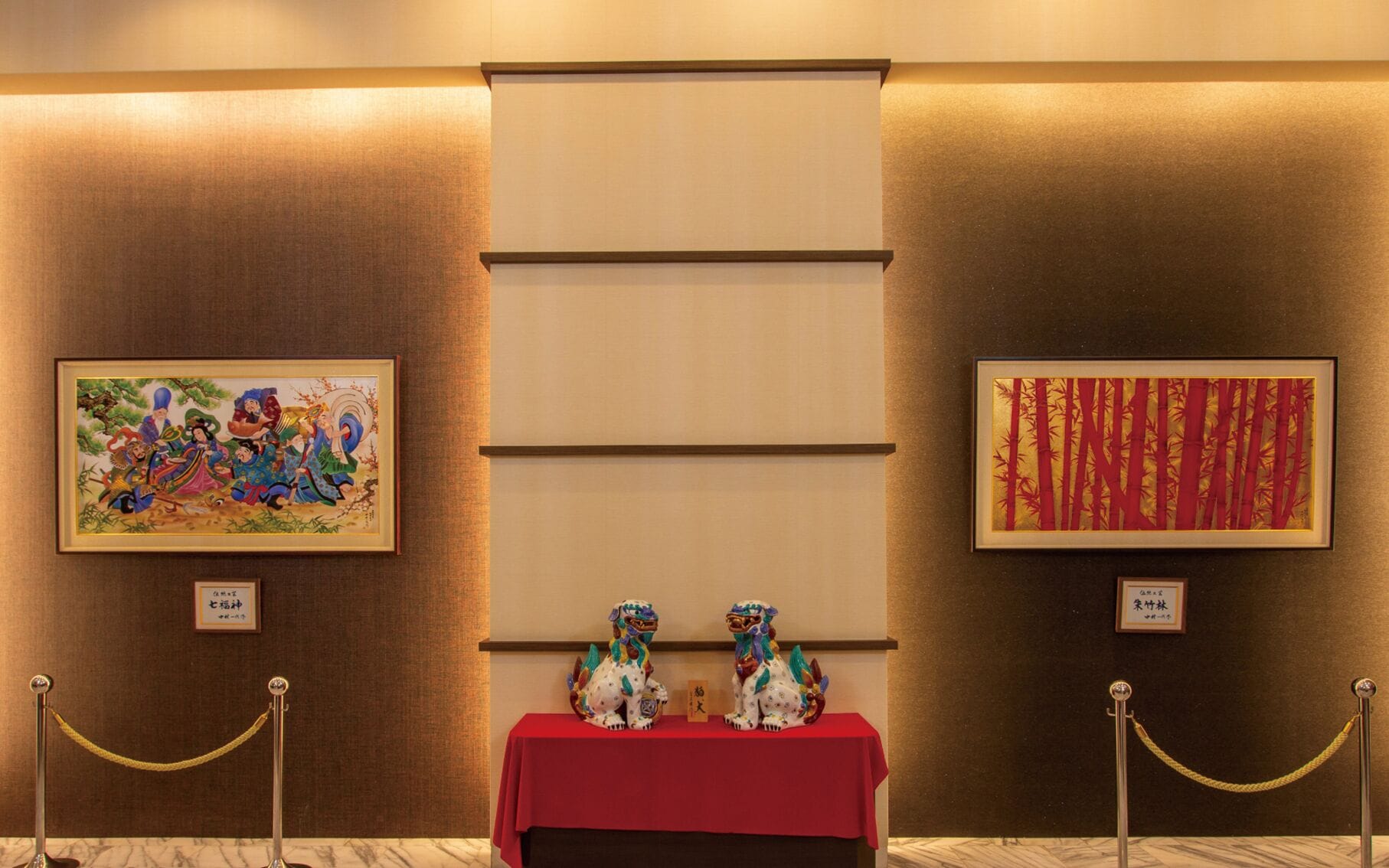 A room with two framed artworks, a red table with two lion statues, and a marble floor.