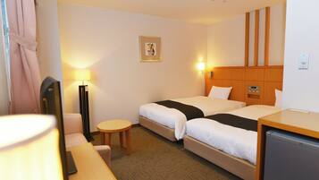 Habitación de hotel con dos camas, un escritorio, una lámpara y una mesita.