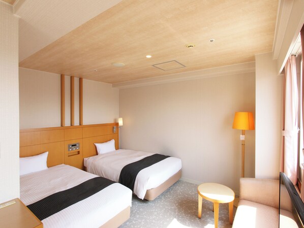 Habitación de hotel con dos camas, una mesita, una lámpara y una ventana con cortinas.