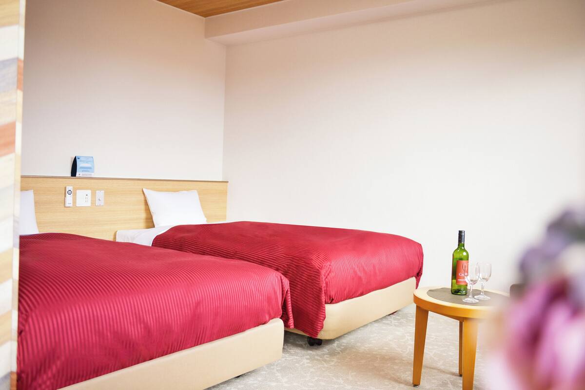 A hotel room with two beds, a small round table with a bottle and glasses, and a wooden headboard.