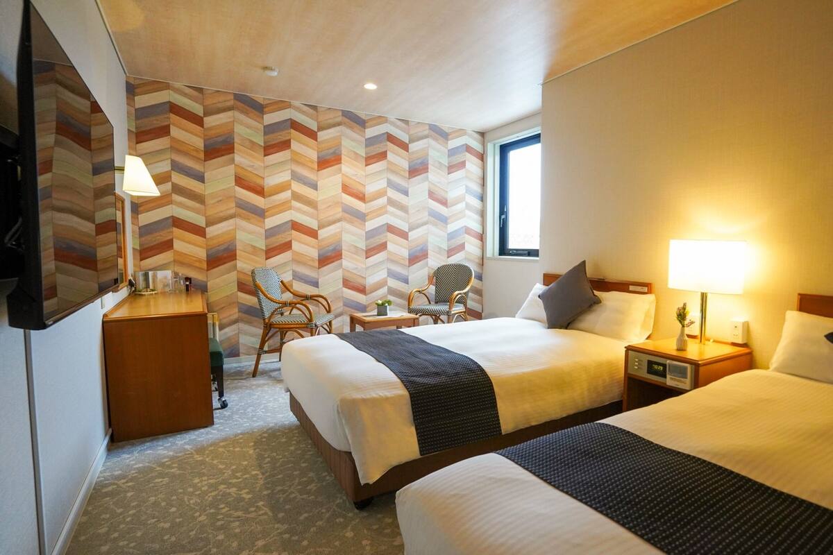 Ett hotellrum med två sängar, ett skrivbord, en stol och en vägg med ett fiskbensmönster.