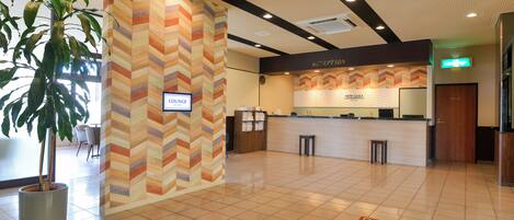 A hotel reception area with a chevron-patterned wall, a reception desk, a lounge sign, and a reception desk with a 'New Gaea' sign.