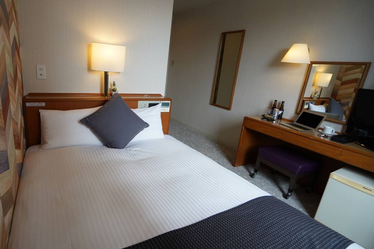 Ett hotellrum med en säng, sänglampor, ett skrivbord med en bärbar dator och en spegel.