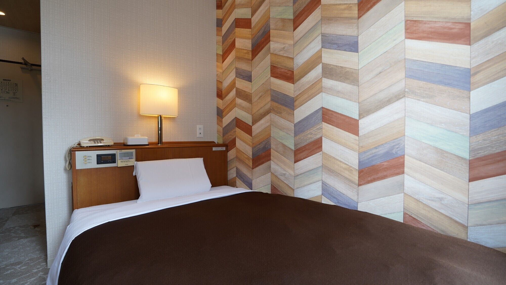 A hotel room with a bed, a nightstand with a lamp, a wall clock, and a telephone.
