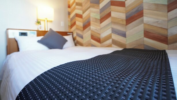 Un lit bien fait, avec une couvre-lit à motifs, un oreiller et une tête de lit dotée d’un écran numérique.