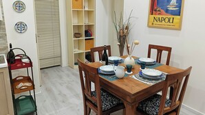 A dining area with a wooden table set for four, surrounded by chairs with patterned cushions. A bookshelf is against the wall, and a poster of Naples is visible. - Piazzetta 4 - Holiday Home (Napoli)