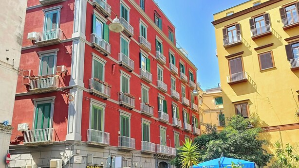 A multi-story building with balconies, a shop with a sign reading "TABACCHI," and outdoor seating under a blue umbrella. - Piazzetta 4 - Holiday Home (Napoli)