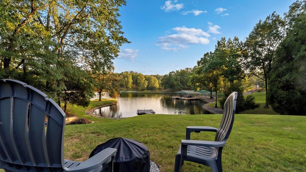 Vista de un lago con dos sillas Adirondack, una parrilla cubierta y un pabellón cerca del agua.