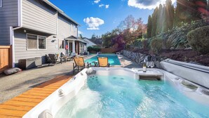 Un patio trasero con un jacuzzi, una terraza de madera y una zona de piscina.