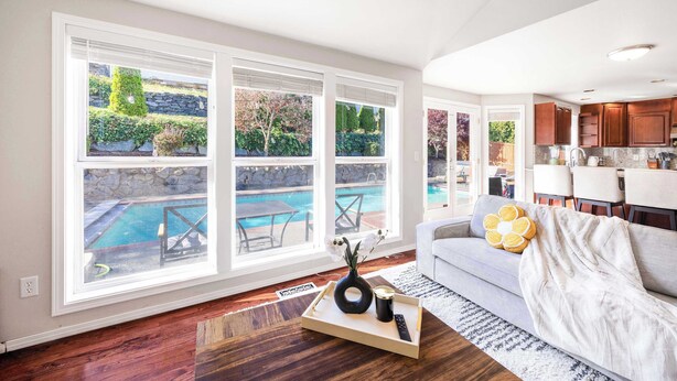 Un amplio salón con grandes ventanales que dan a una piscina y un jardín.