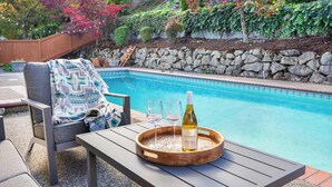 Escena junto a la piscina con una mesa de madera, dos vasos y una botella de vino sobre una bandeja.