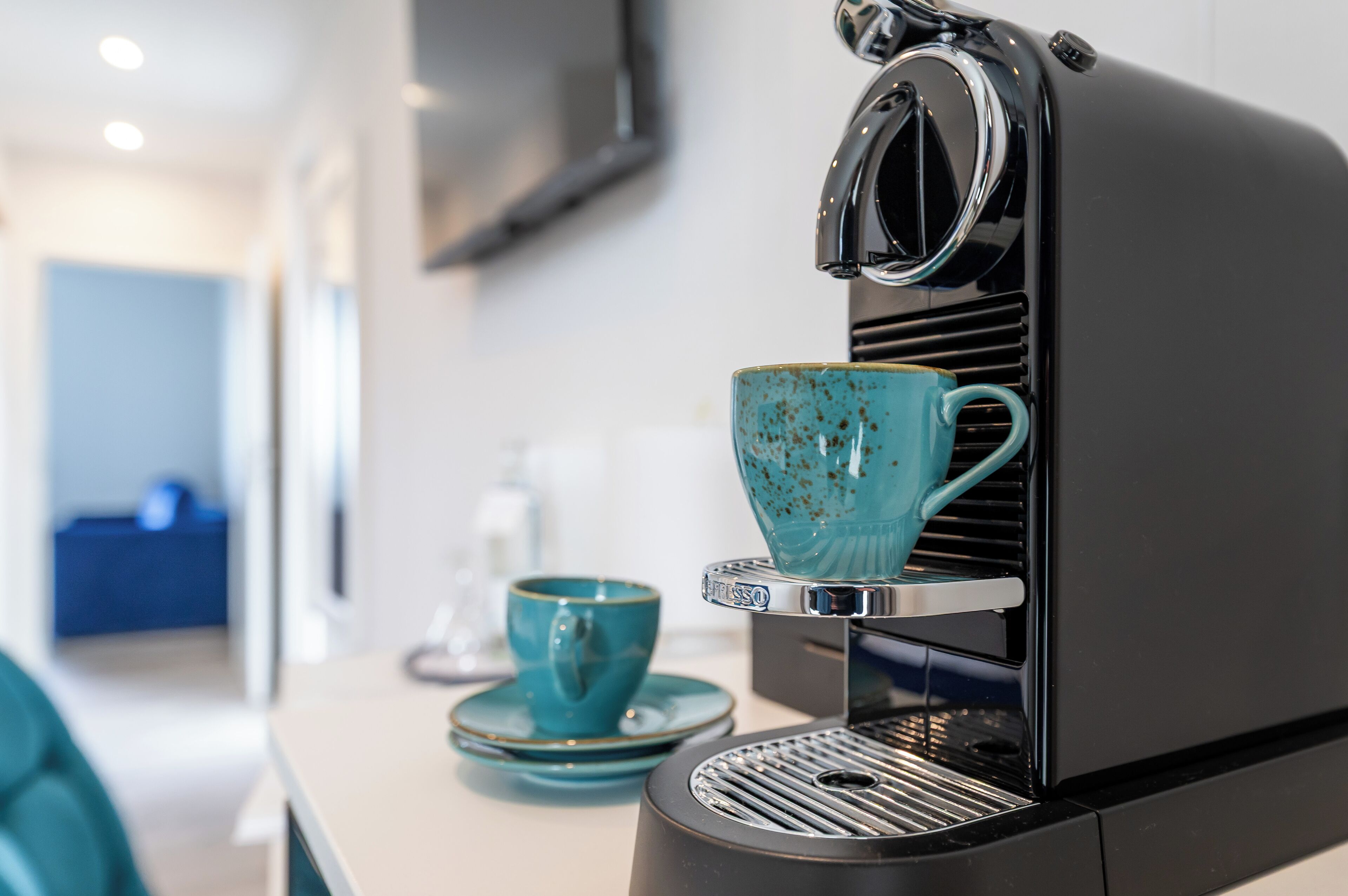 A compact espresso machine with a teal cup and saucer on its drip tray.