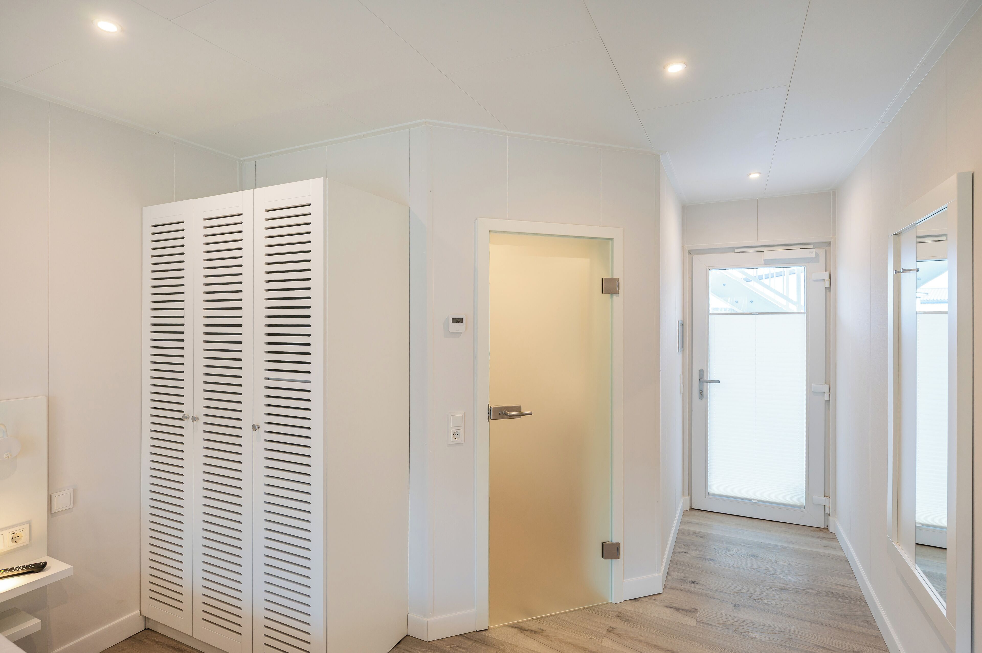 Ein heller, moderner Flur mit einem weißen Schrank, einer Tür zu einem anderen Raum und einem Fenster mit Blick.