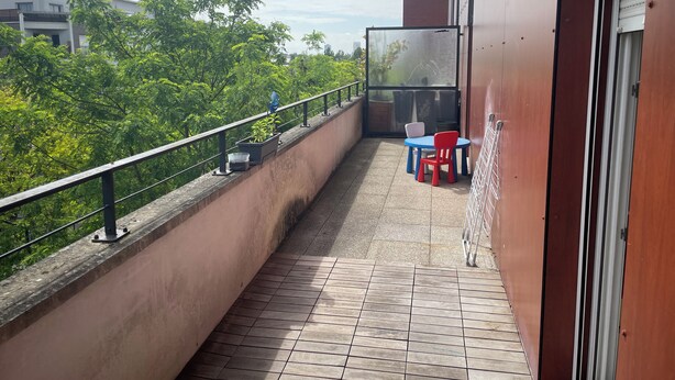 Een balkon met betegelde vloer, een hekwerk en een tafel met stoelen.