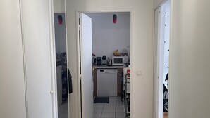 Een gang met een houten vloer die uitkomt in een keuken met een magnetron, koffiezetapparaat en andere apparaten.