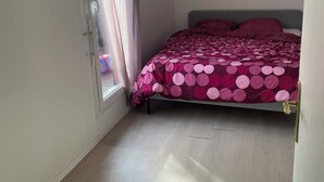 Een slaapkamer met een bed, een raam met gordijnen en een houten vloer.