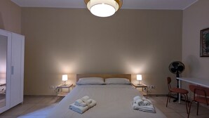 A hotel room with a bed, two bedside lamps, a ceiling fan, and a desk with chairs.