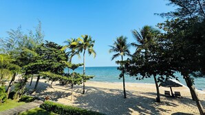 A beach with palm trees, a wooden walkway, and a beach umbrella.