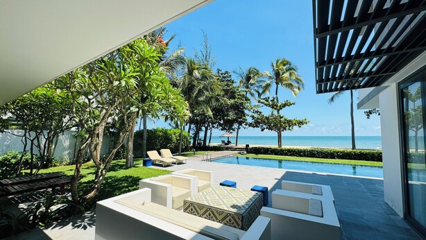 A modern outdoor lounge area with a pool, seating, and a view of the ocean.