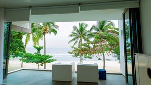 A modern room with large windows overlooking a beach, featuring two white sofas and a blue ottoman.