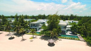 A beachfront property with modern villas, a swimming pool, and palm trees.