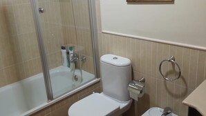 Un baño con ducha, inodoro, bidé y dos cuadros en la pared.