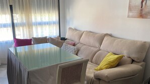 Una sala de estar con un sofá color beige, una mesa de comedor con superficie de vidrio y una silla.