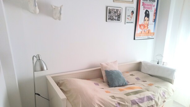 Un dormitorio con una cama, una lámpara de pie y adornos en la pared, incluyendo fotografías y carteles enmarcados.