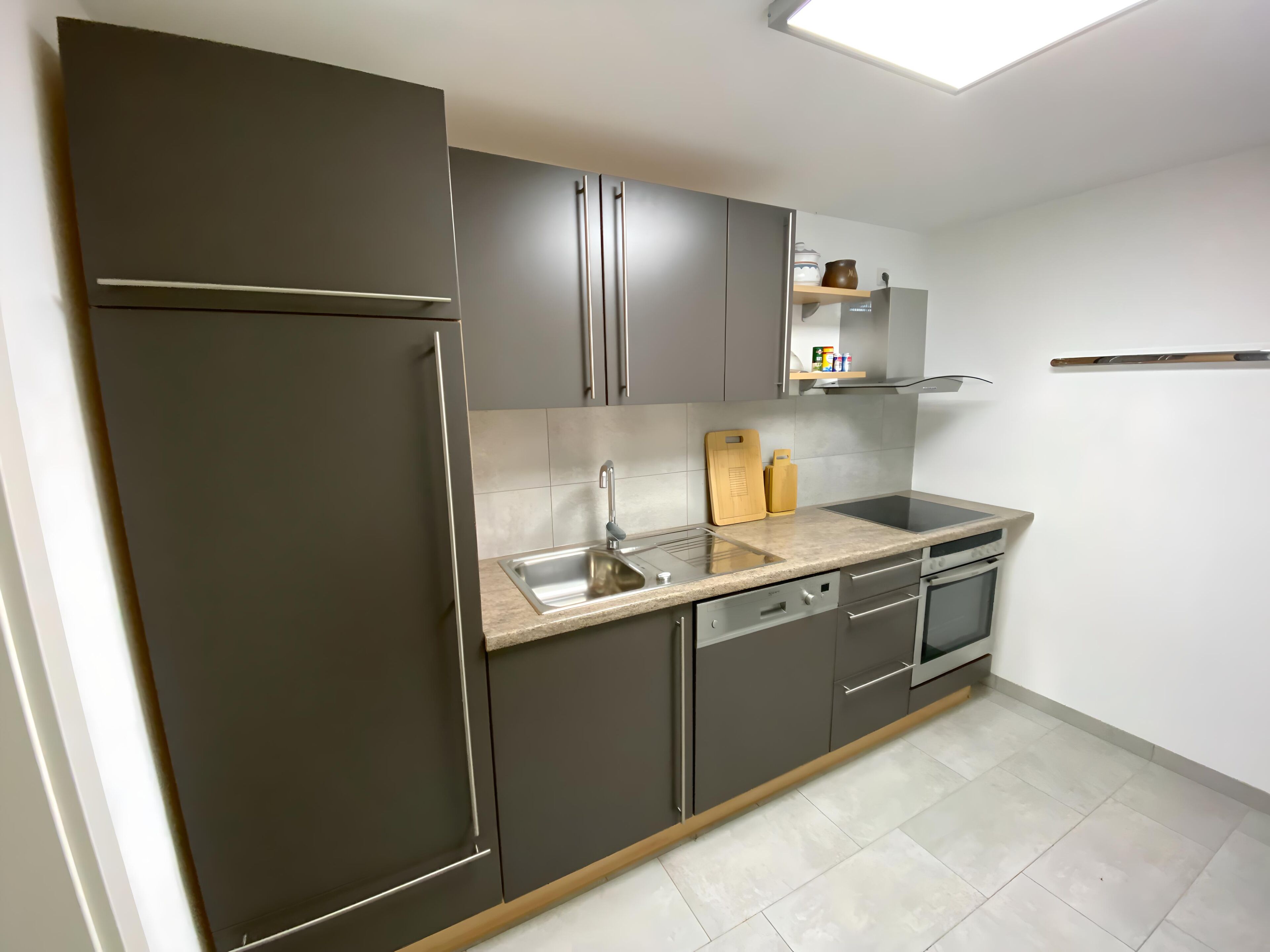 Una cucina moderna con mobili scuri, un lavello in acciaio inossidabile e un forno integrato.