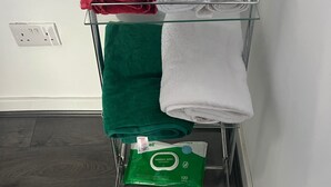 A metal towel rack with three folded towels in red, white, and green, and a pack of universal wipes on the bottom shelf.
